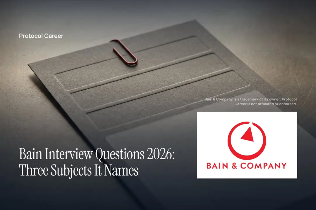 A heavy cardstock rubric with three debossed rows and a red clip rests on a graphite desk. Title: “Bain Interview Questions 2026: Three Subjects It Names”, over the Protocol Career wordmark. Bain & Company logo, lower right.